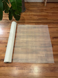 Roll of white mosaic mesh on a wooden floor with a plant in the corner