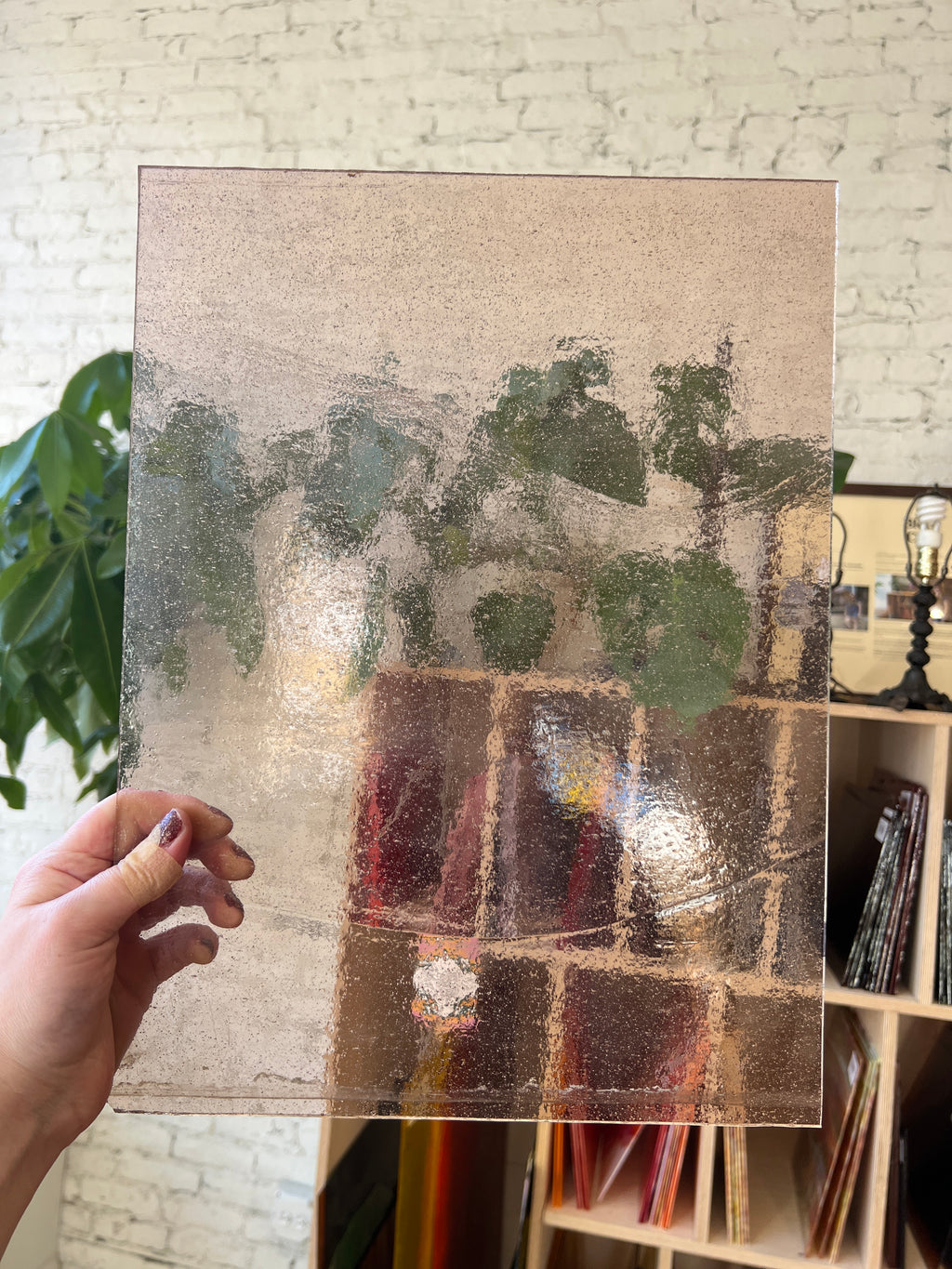Hand holding a textured transparent blush colored piece of stained glass in front of a colorful shelf