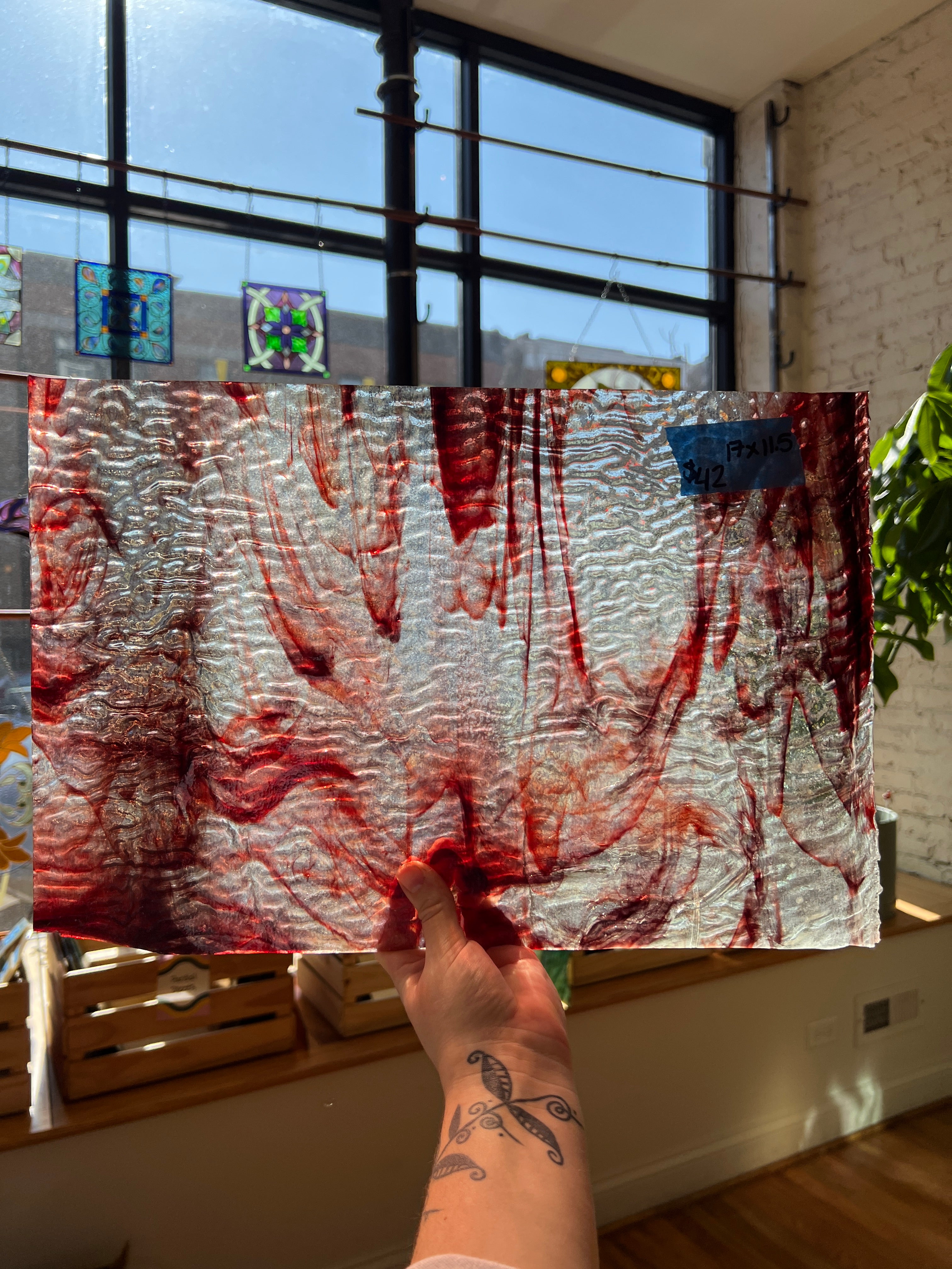 Person holding a large textured piece of glass with red and white patterns in front of a window.
