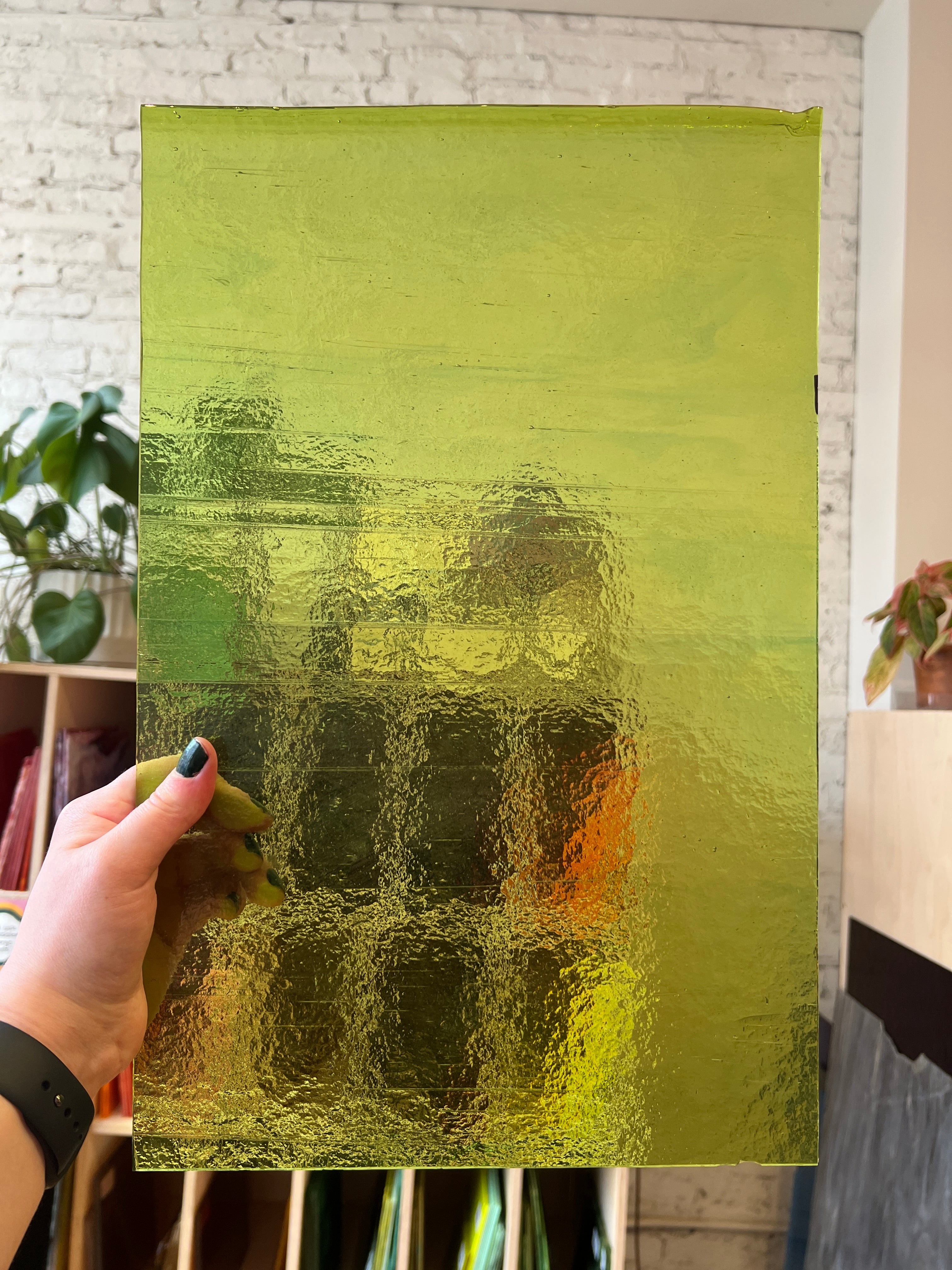 Person holding a green textured piece of glass in front of shelves