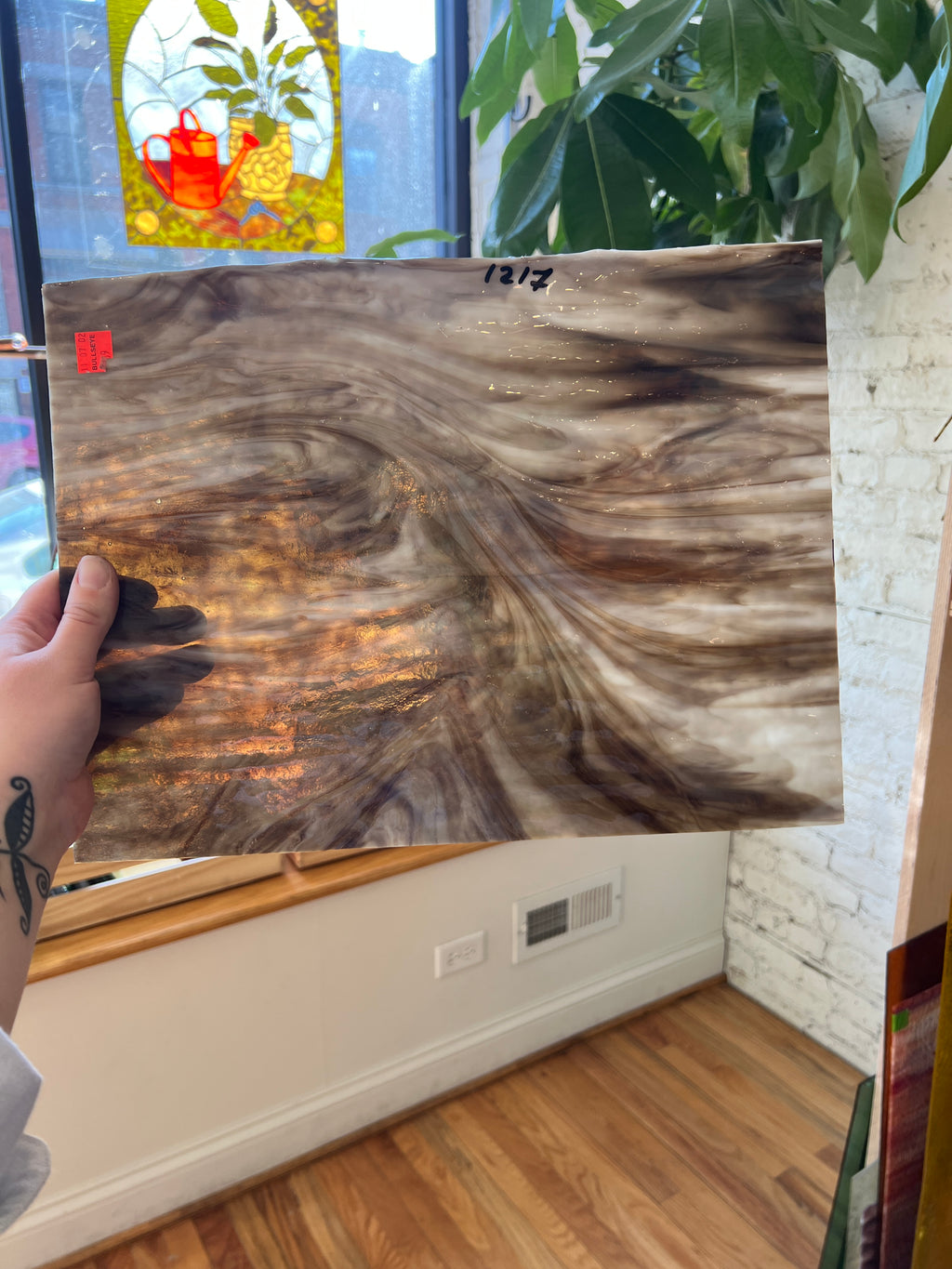 Person holding a piece of brown and white swirled stained glass in front of a blurred interior background 