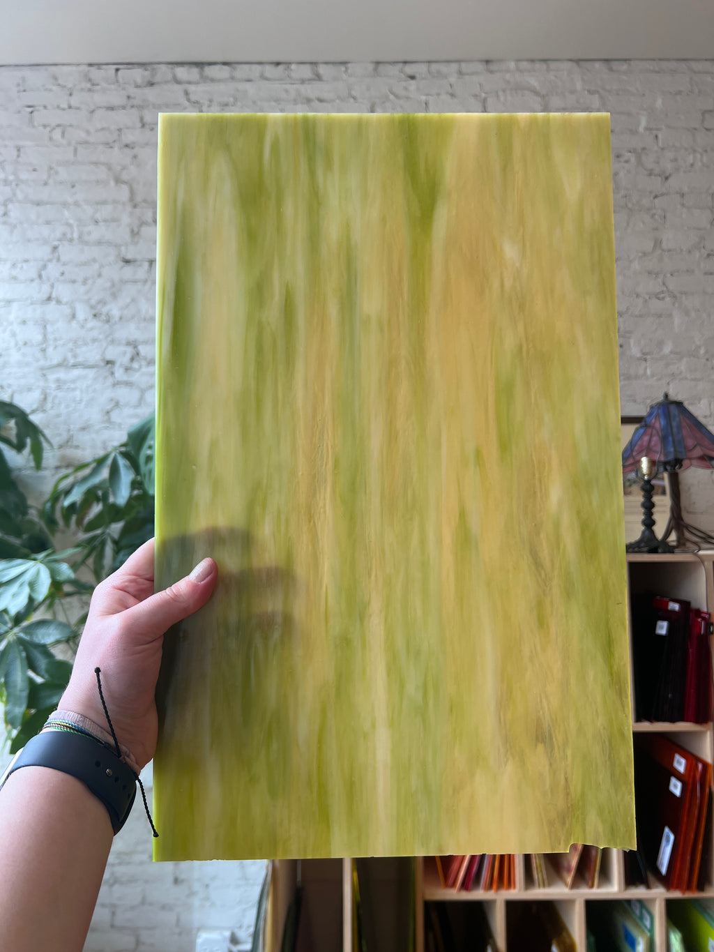 Hand holding a large green marbled sheet of stained glass against a blurred indoor background
