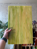 Hand holding a large green marbled sheet of stained glass against a blurred indoor background