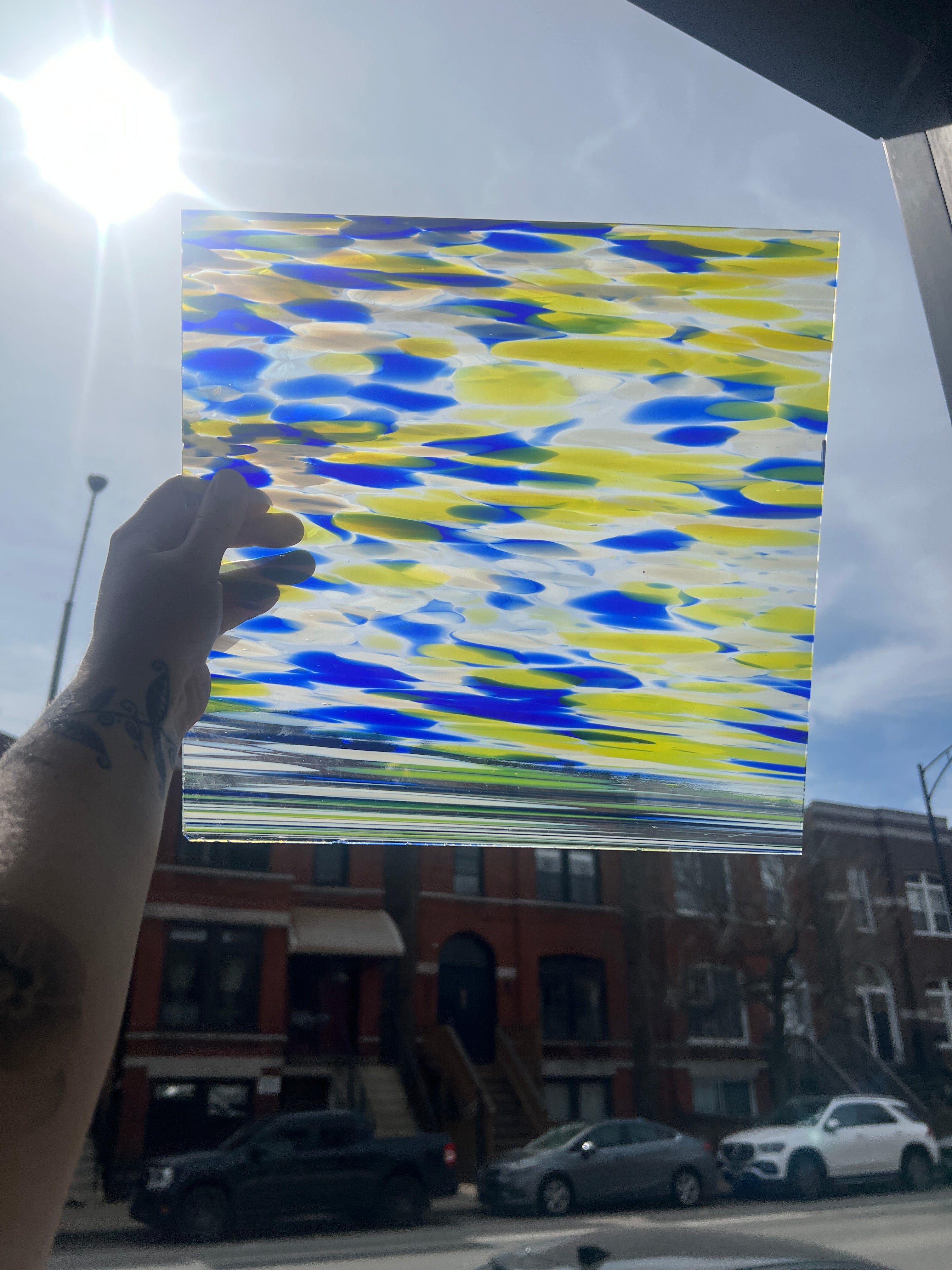 Hand holding a colorful piece of stained glass with a city street in the background