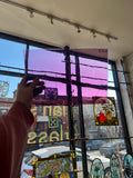 Person taking a photo of purple stained glass art in a store window