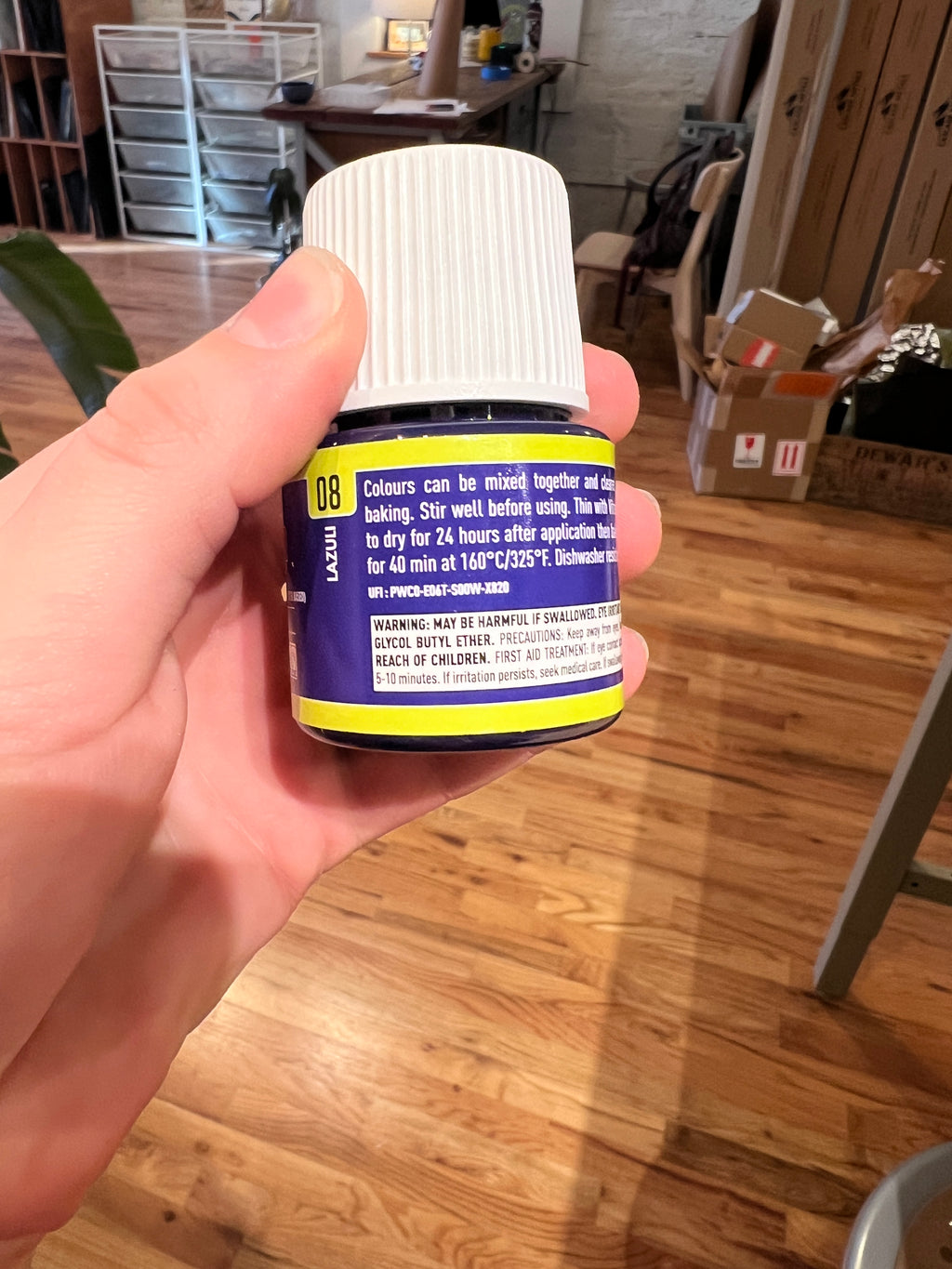 Hand holding a cylindrical product with a blue label in an indoor setting