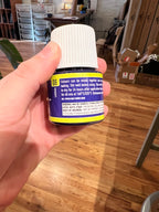 Hand holding a cylindrical product with a blue label in an indoor setting