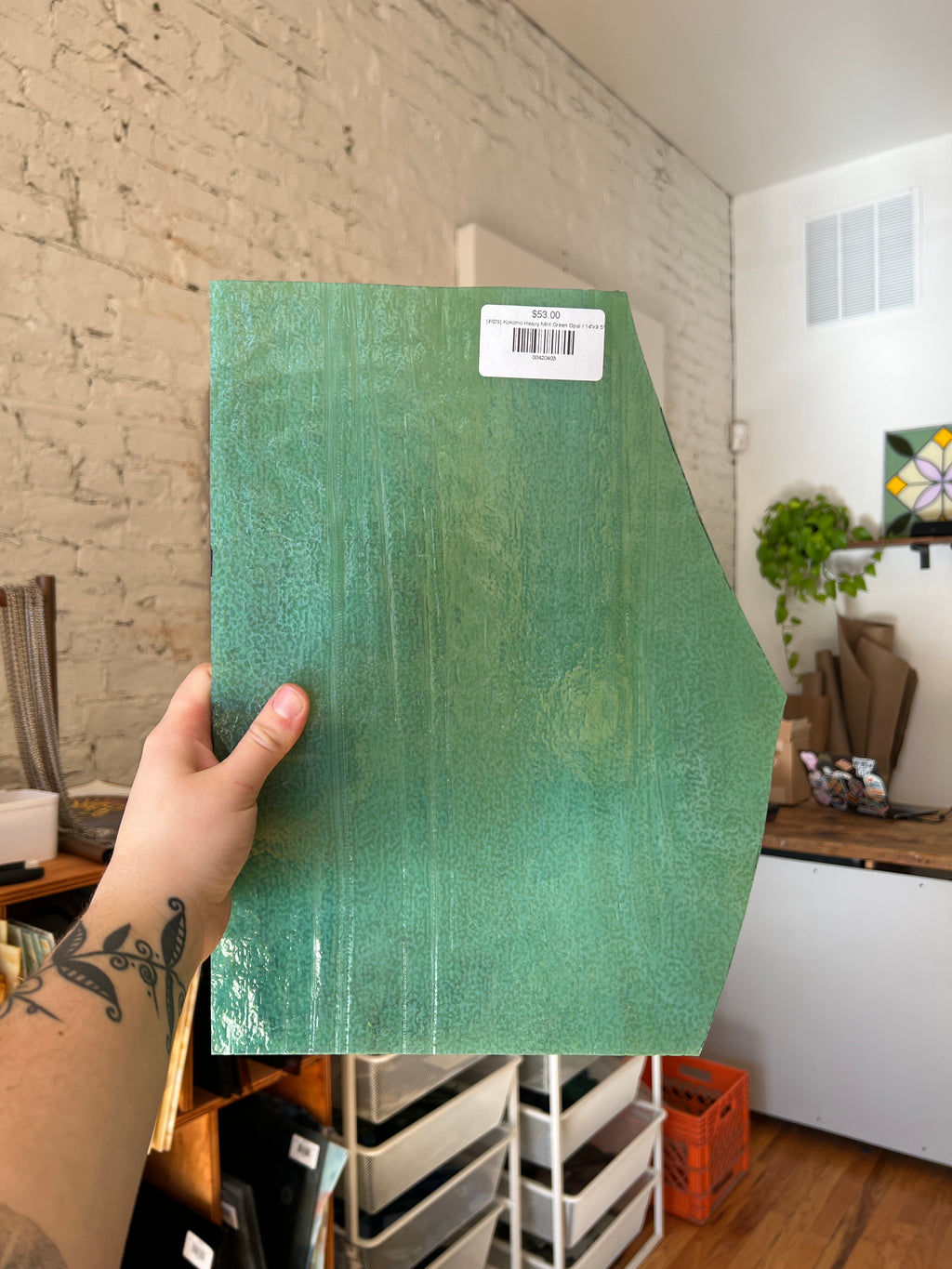 Person holding a green piece of stained glass with a barcode label in an indoor setting