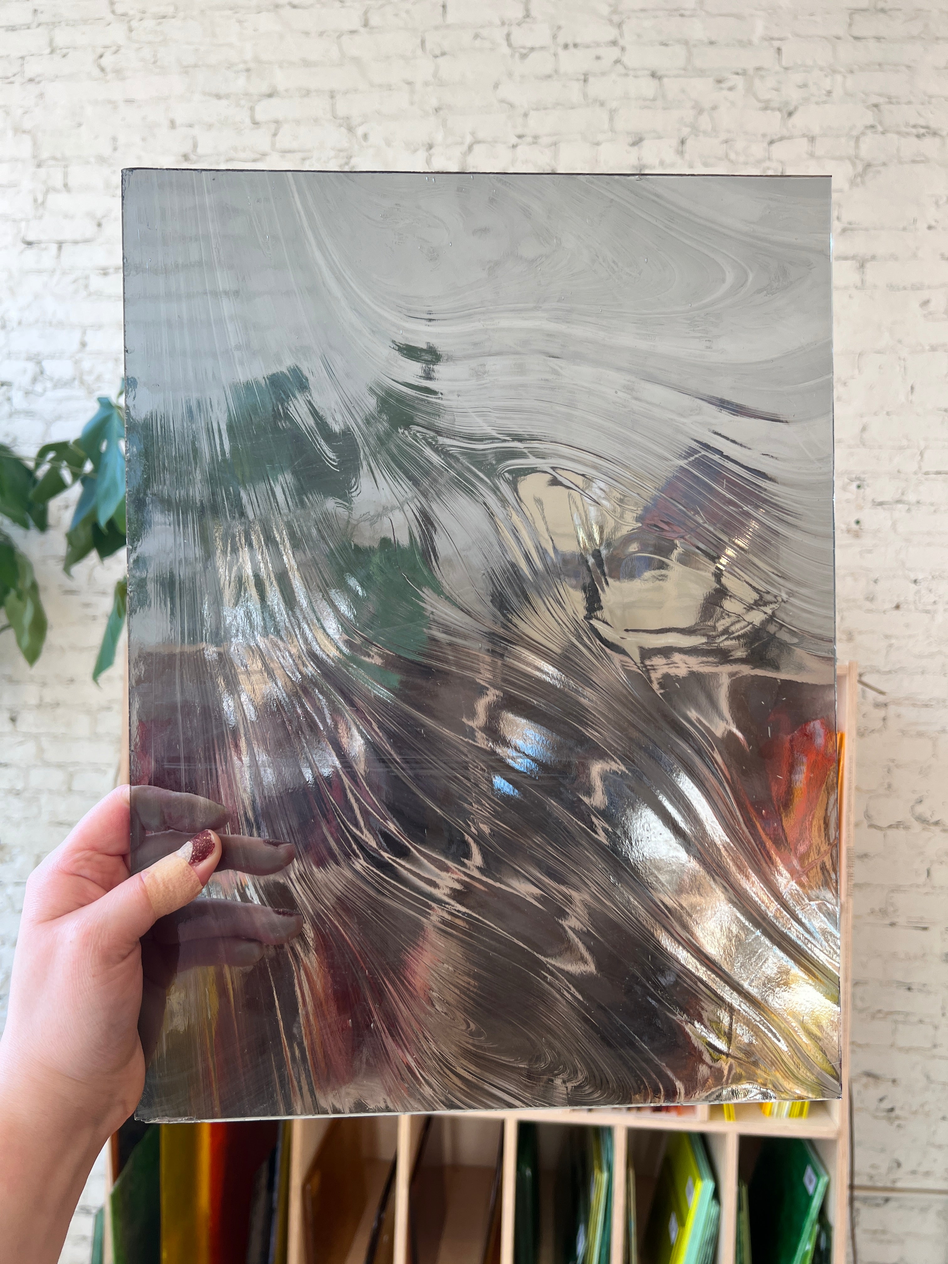 Person holding a piece of grayish swirled slightly transparent stained glass against a textured wall.