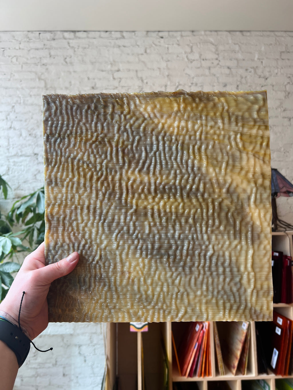 Hand holding a textured sheet of brown stained glass with a wavy pattern against a neutral background