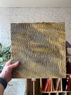 Hand holding a textured sheet of brown stained glass with a wavy pattern against a neutral background