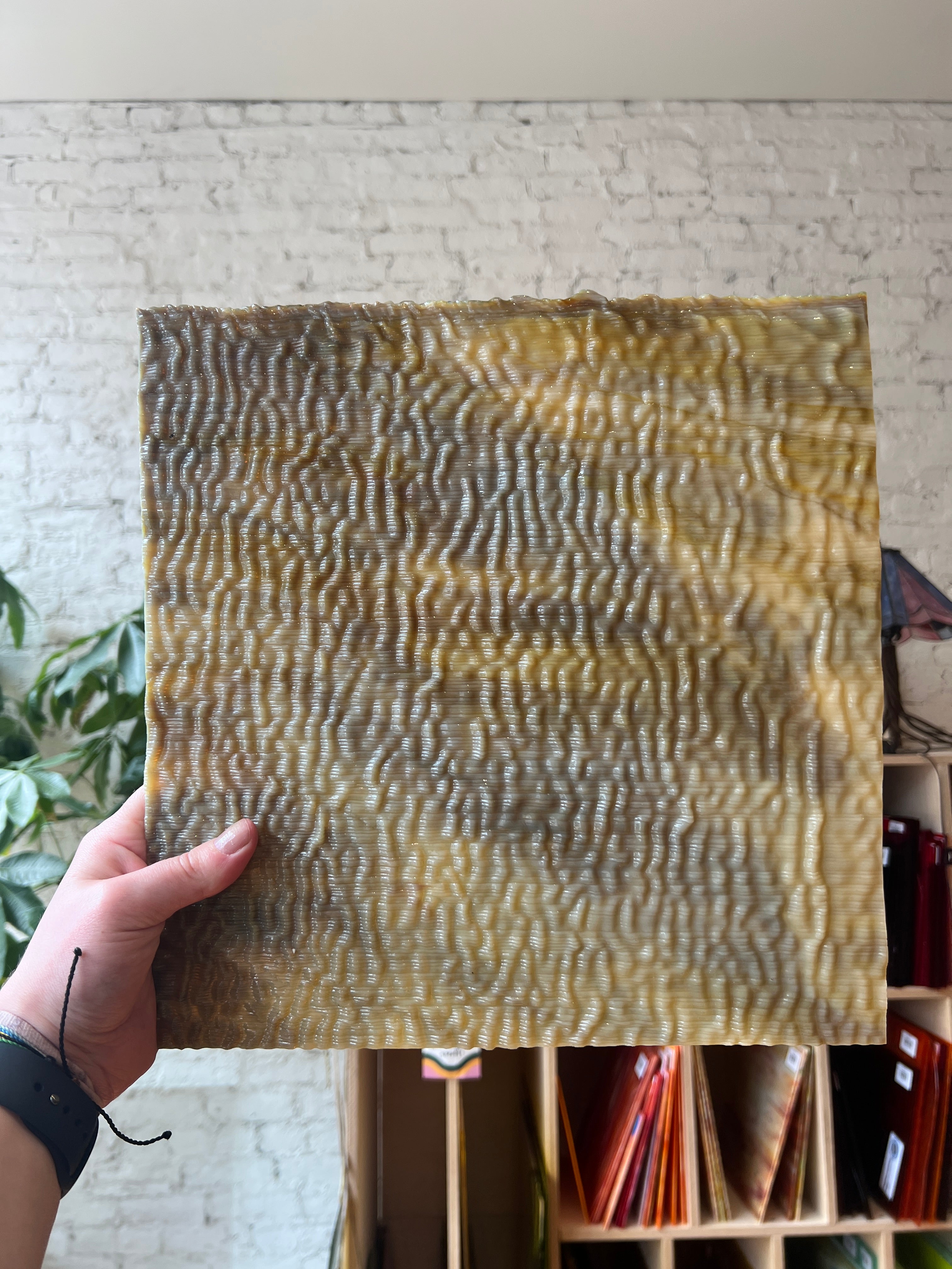 Hand holding a textured sheet of brown stained glass with a wavy pattern against a neutral background