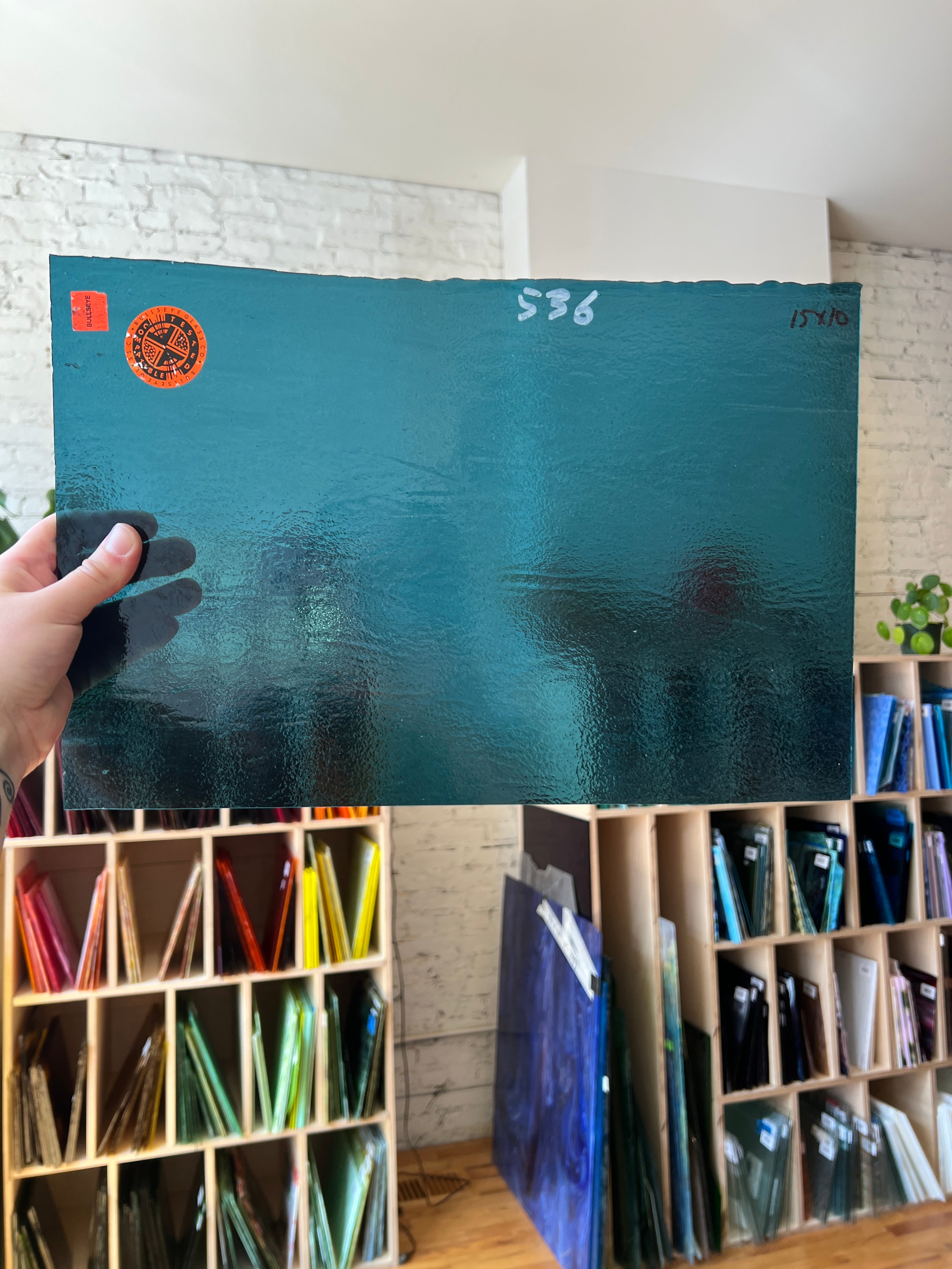 Teal piece of glass with orange label held by a hand, surrounded by sheets of glass in a box.