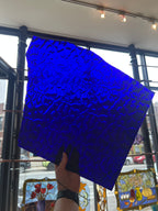 Blue textured panel of glass held by a person in front of a stained glass window