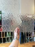 Person holding a clear textured panel of stained glass in a workshop setting. 