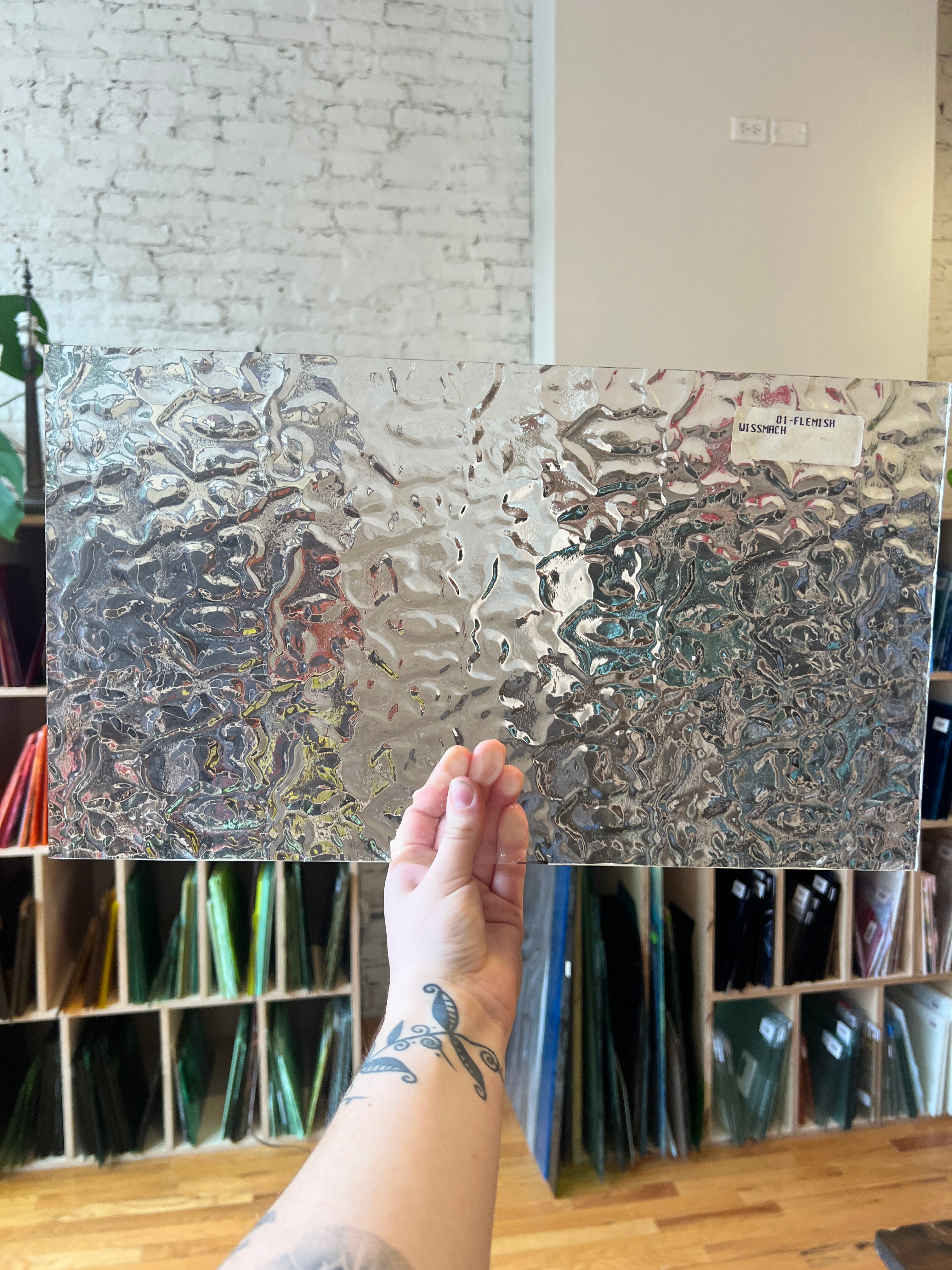 Person holding a clear textured panel of stained glass in a workshop setting. 
