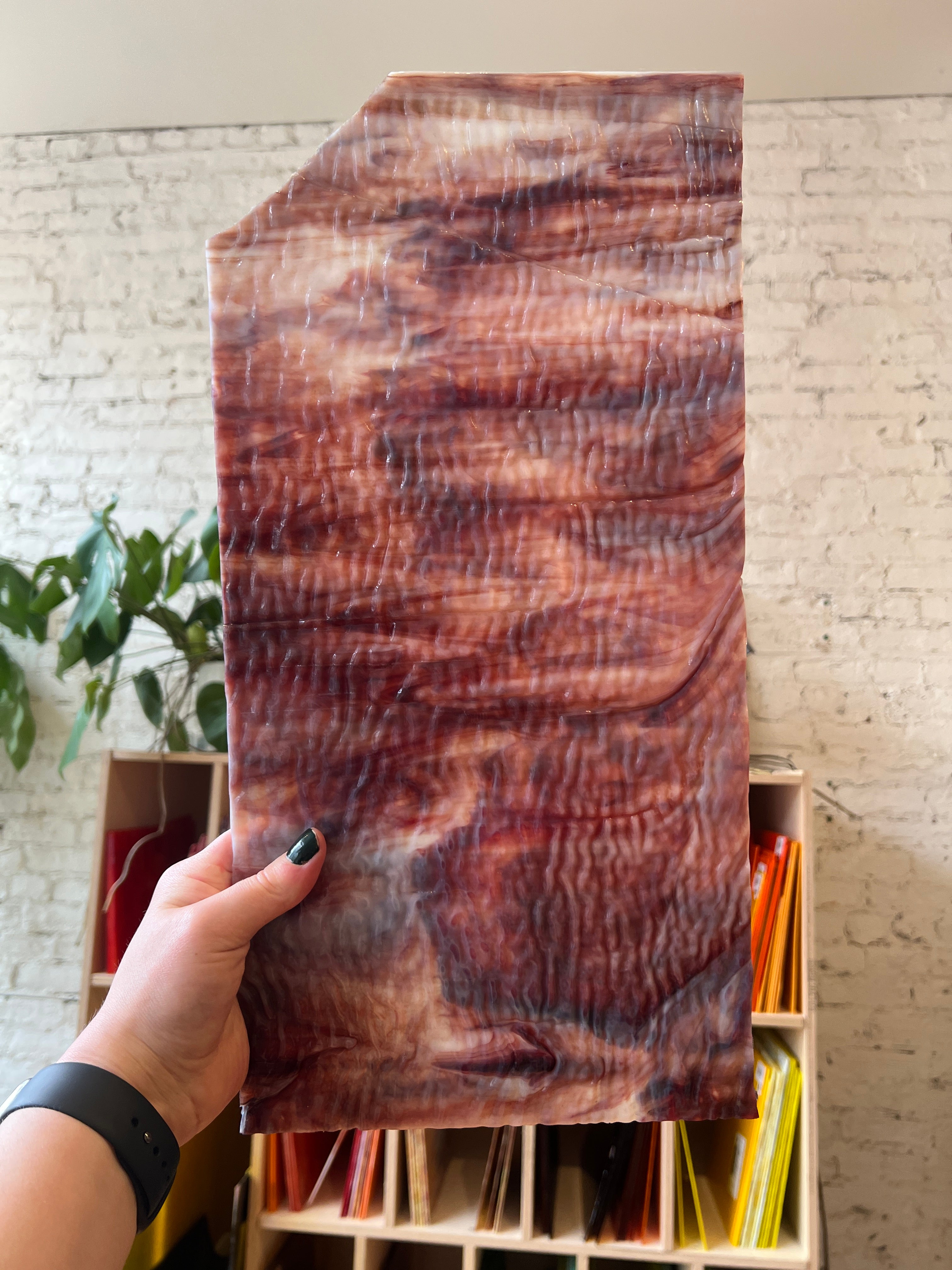 Person holding a swirled red piece of glass with a textured surface, against a neutral background.