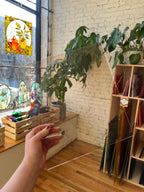 Hand holding a piece of transparent lightly textured brownish glass in front of a plant and interior decor in the background