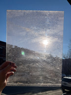 Hand holding a rectangular piece of textured transparent glass against a blue sky.