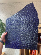 Textured blue panel of glass held by a hand against a neutral background