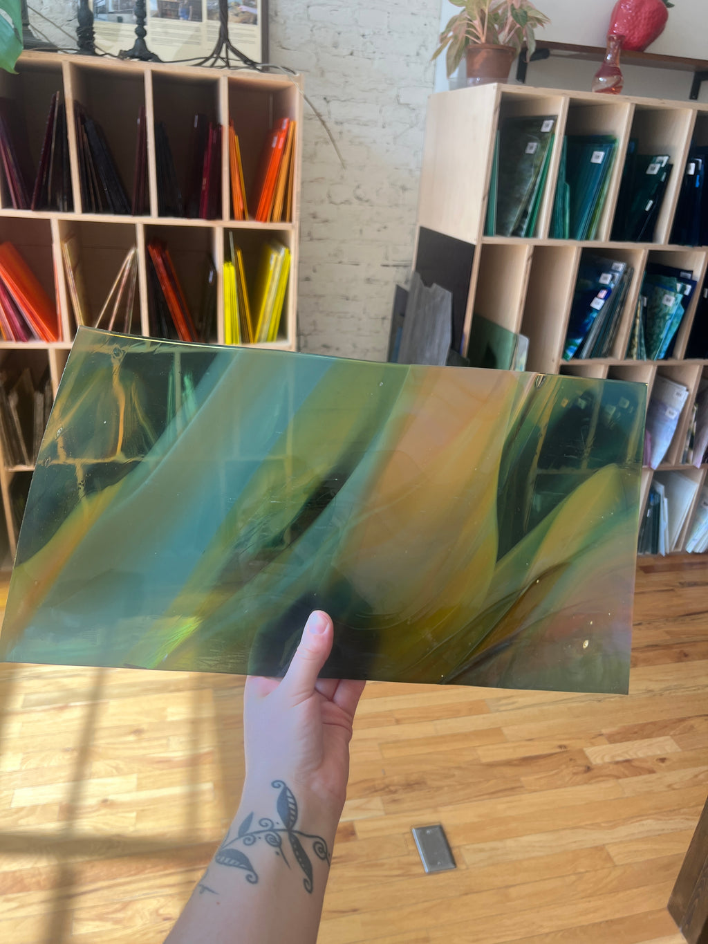 Person holding a green and yellow swirled piece of stained glass in a room with bookshelves.