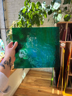 Person holding a green textured piece of stained glass in front of a blurred sunny interior. 
