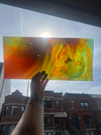 Hand holding a colorful swirled piece of stained glass against a cityscape background