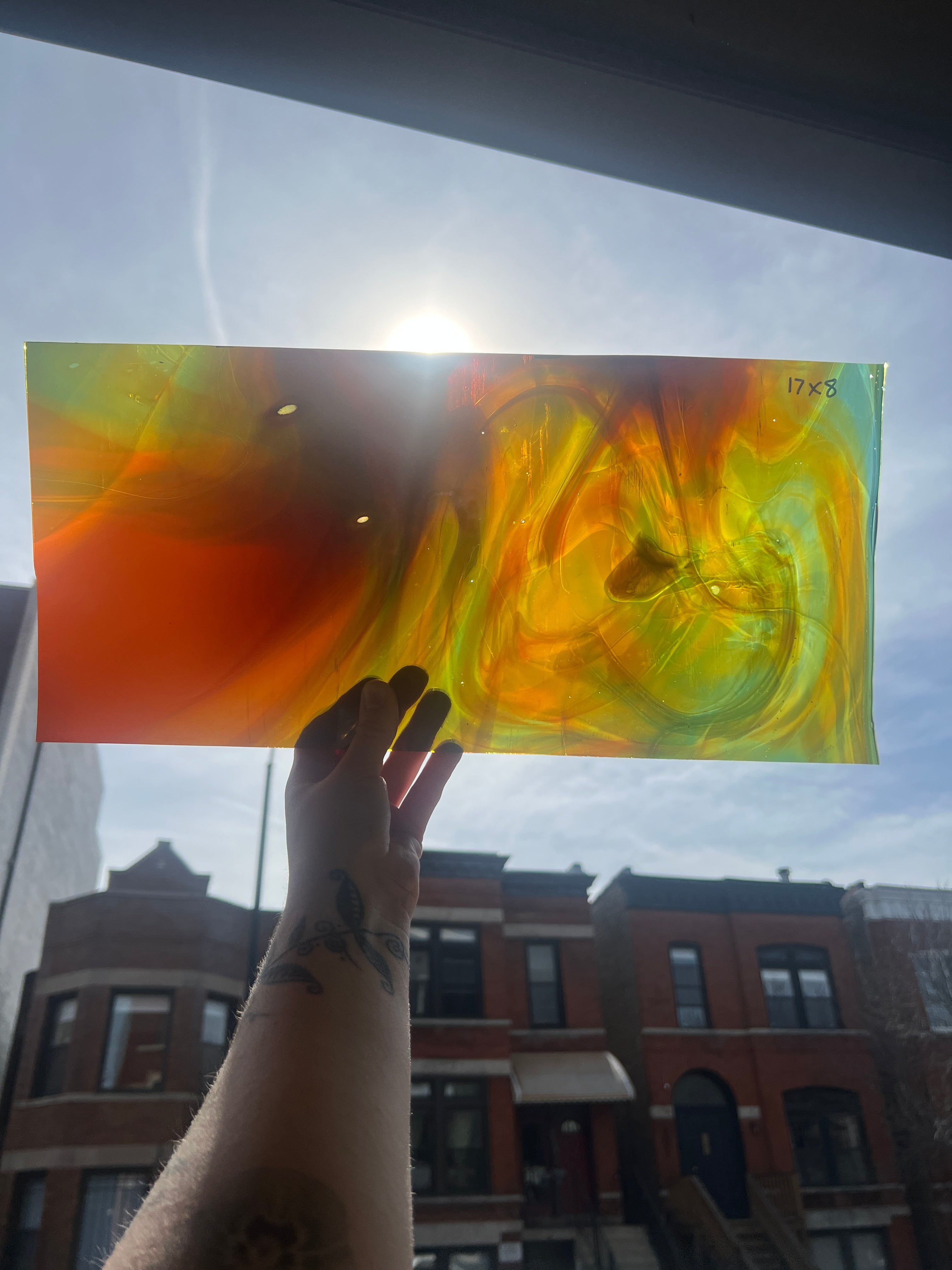 Hand holding a colorful swirled piece of stained glass against a cityscape background