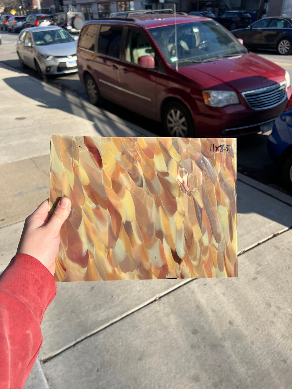 Person holding a colorful abstract piece of stained glass on a city street with cars and buildings in the background.