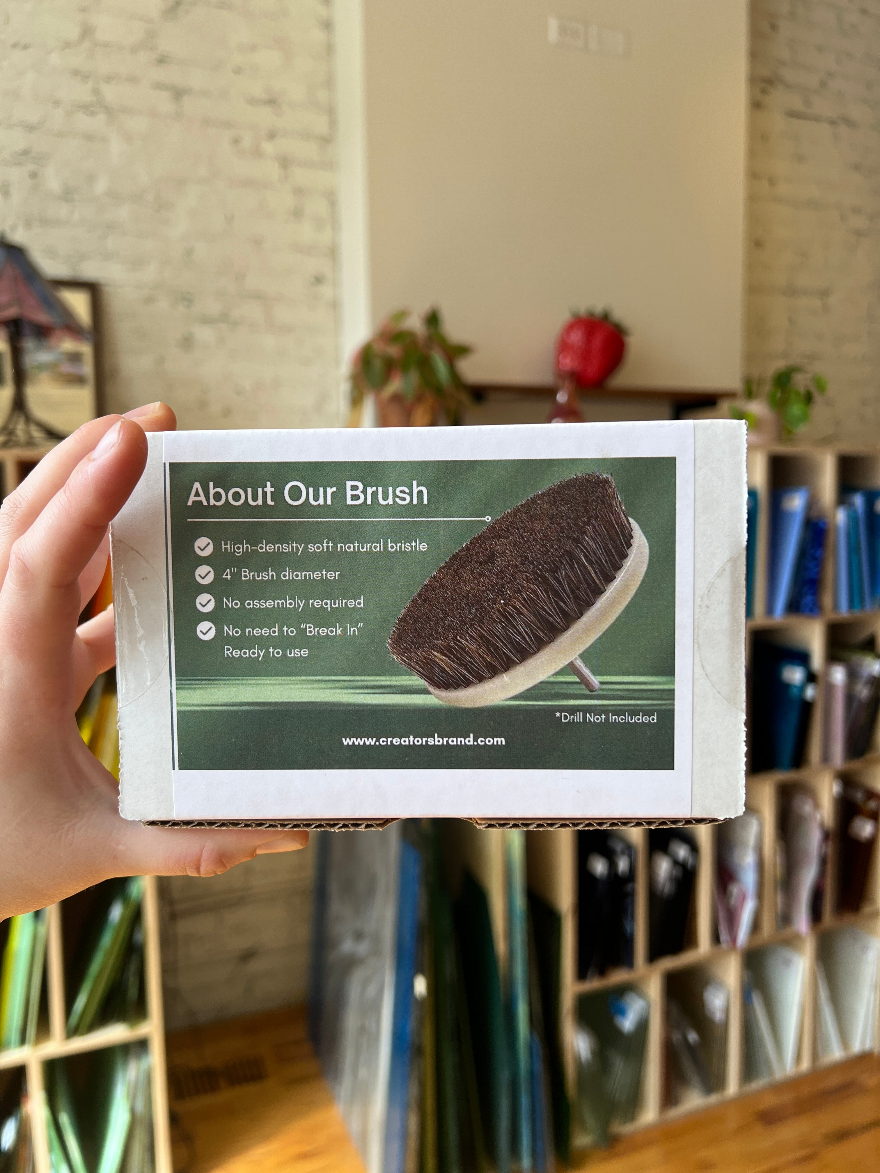 Hand holding a product packaging with a brush image and text.