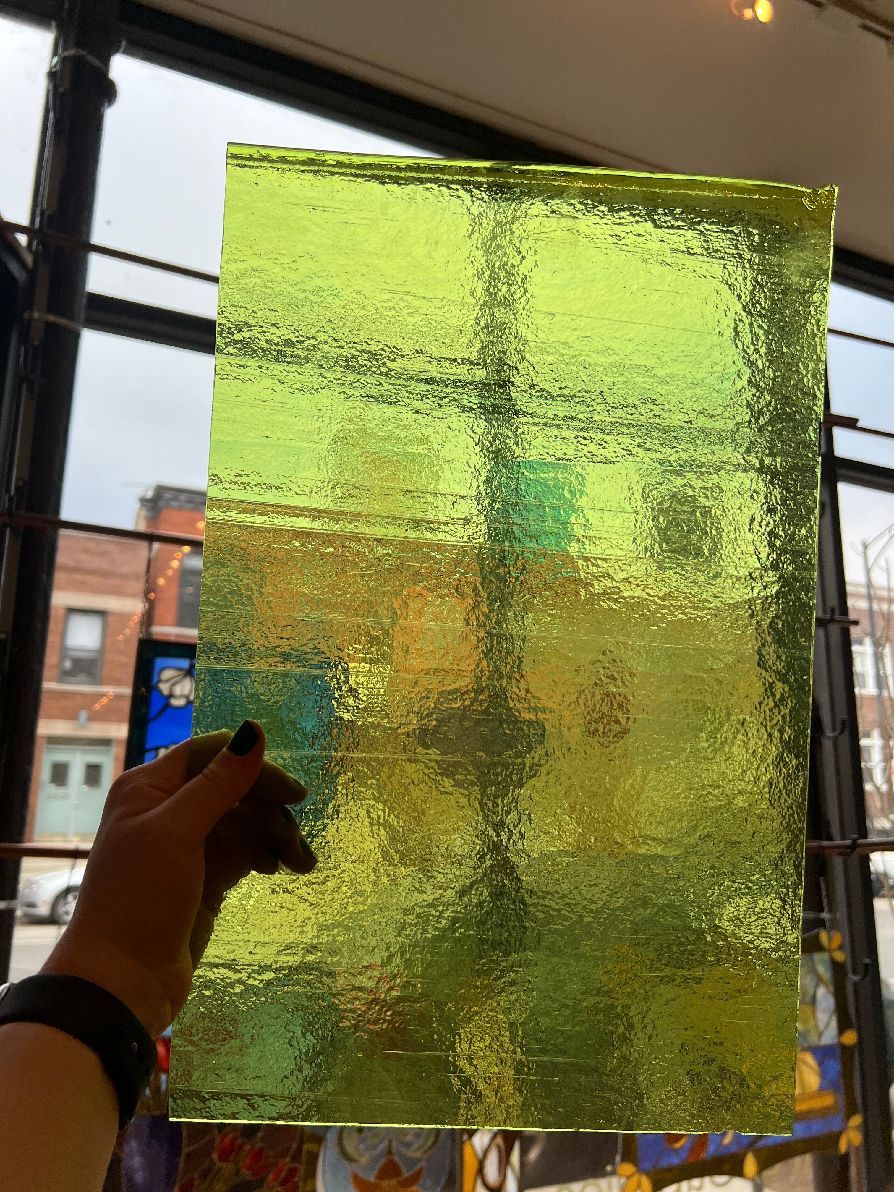 Hand holding a textured green piece of glass with a blurred background