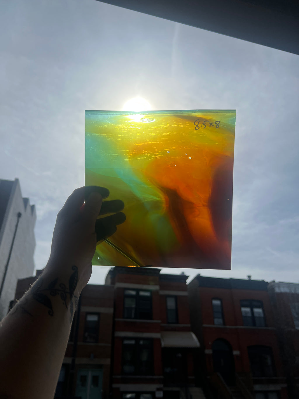 Hand holding a colorful glass panel with a building and sky in the background
