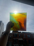 Hand holding a colorful glass panel with a building and sky in the background