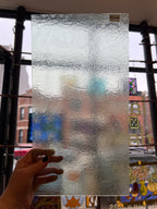 Hand holding a sheet of frosted textured glass film against a window