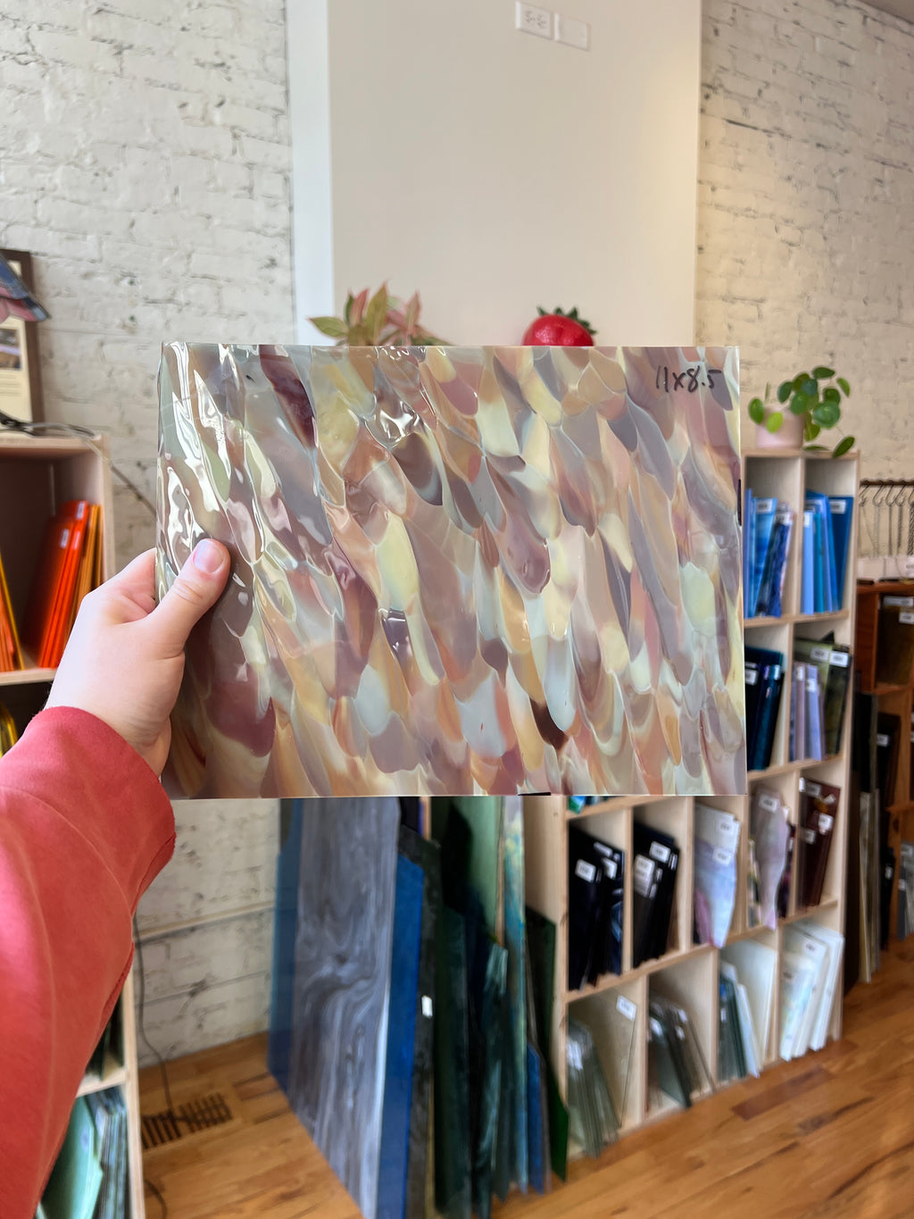 Person holding a colorful piece of stained glass with a bookshelf in the background