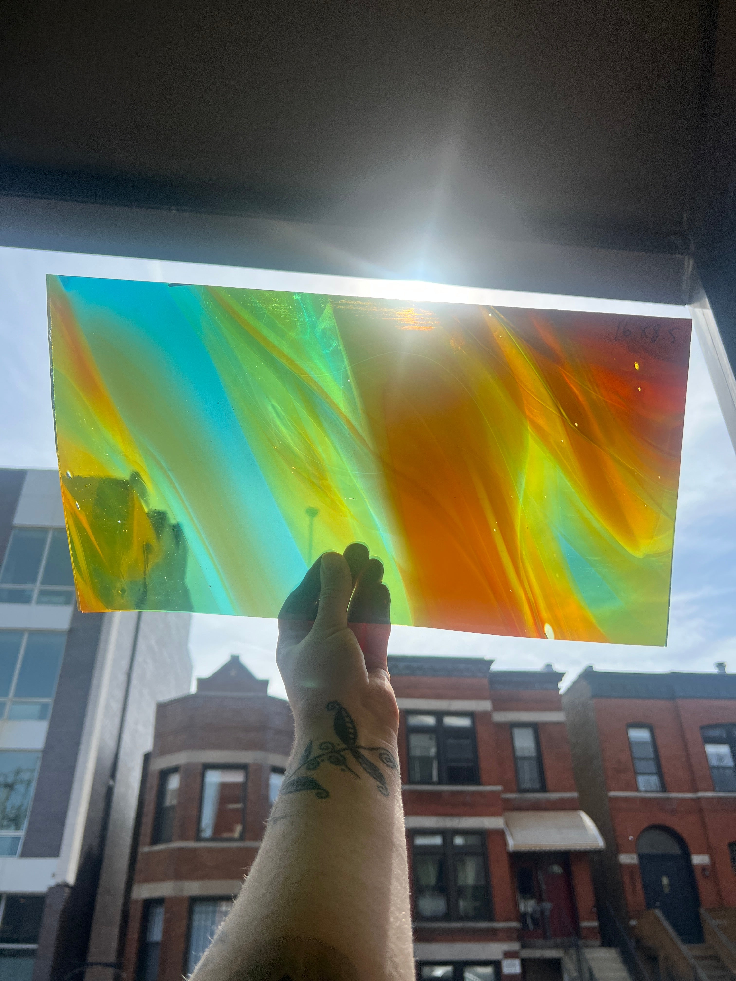 Colorful piece of swirled stained glass held up to a window with buildings in the background