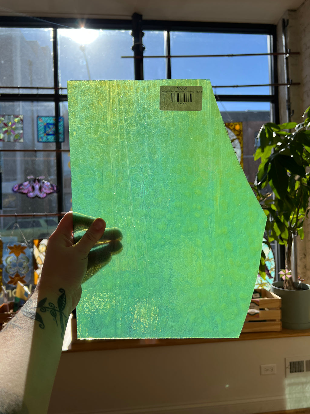 Hand holding a green piece of stained glass in front of a window with sunlight streaming through.