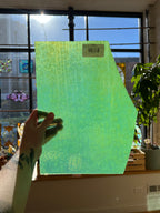 Hand holding a green piece of stained glass in front of a window with sunlight streaming through.