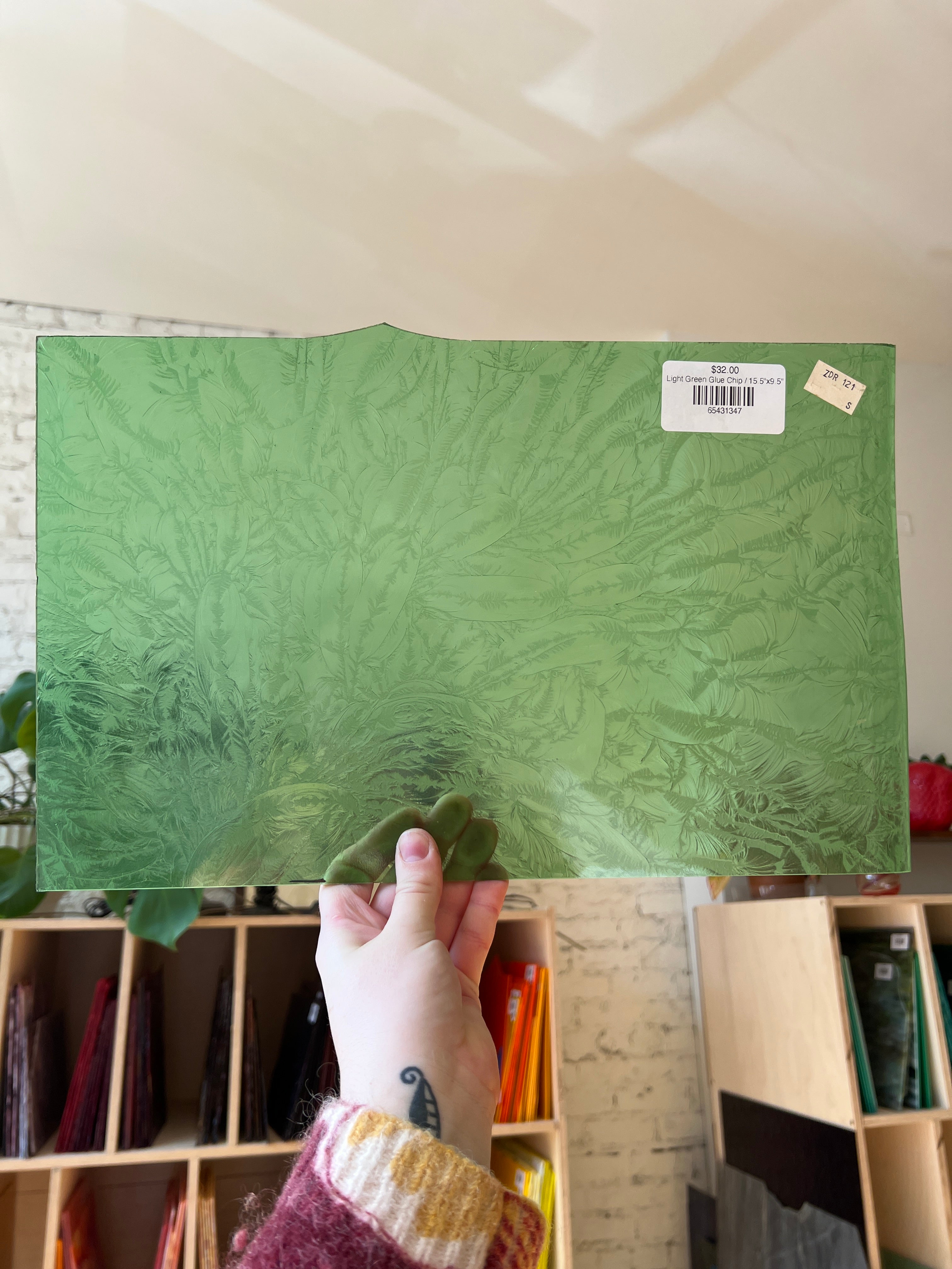 Hand holding a green textured piece of glass with a blurred indoor background