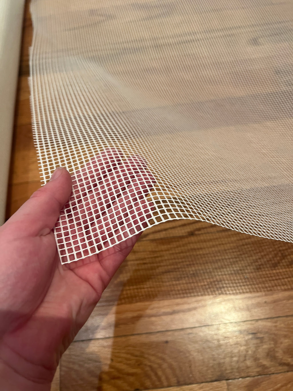 Hand holding a piece of white mesh against a wooden surface