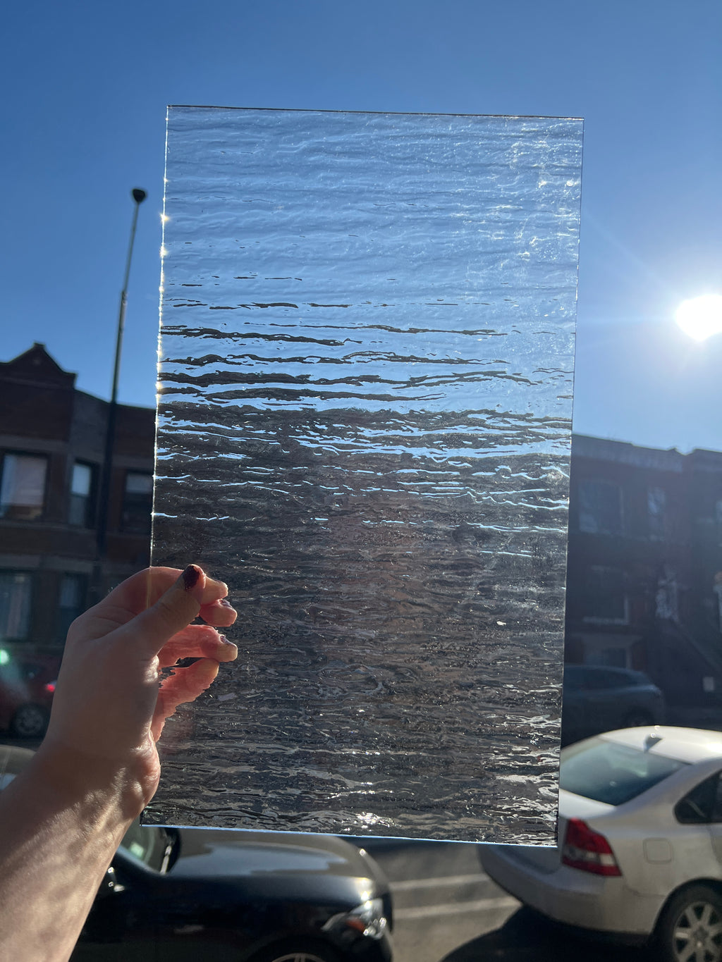 Person holding a sheet of textured clear glass with a blurred street in the background