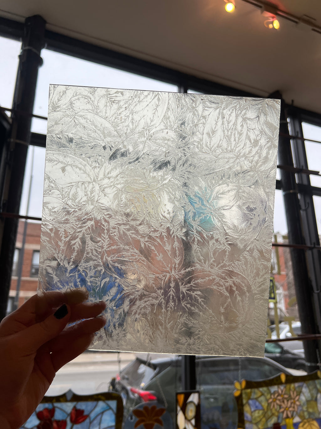 Hand holding a textured piece of stained glass against a blurred indoor background