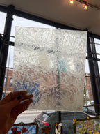 Hand holding a textured piece of stained glass against a blurred indoor background