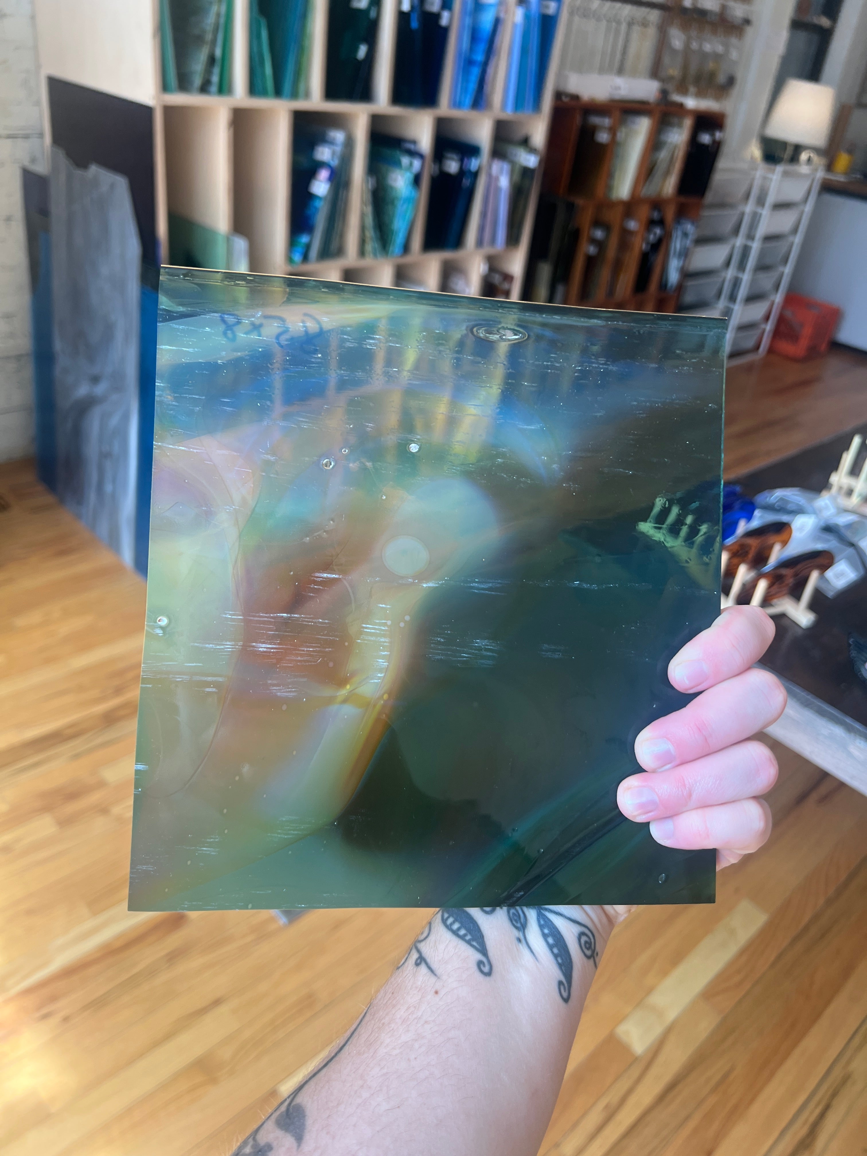 Person holding a transparent sheet of stained glass with a colorful design in a room with books and furniture.