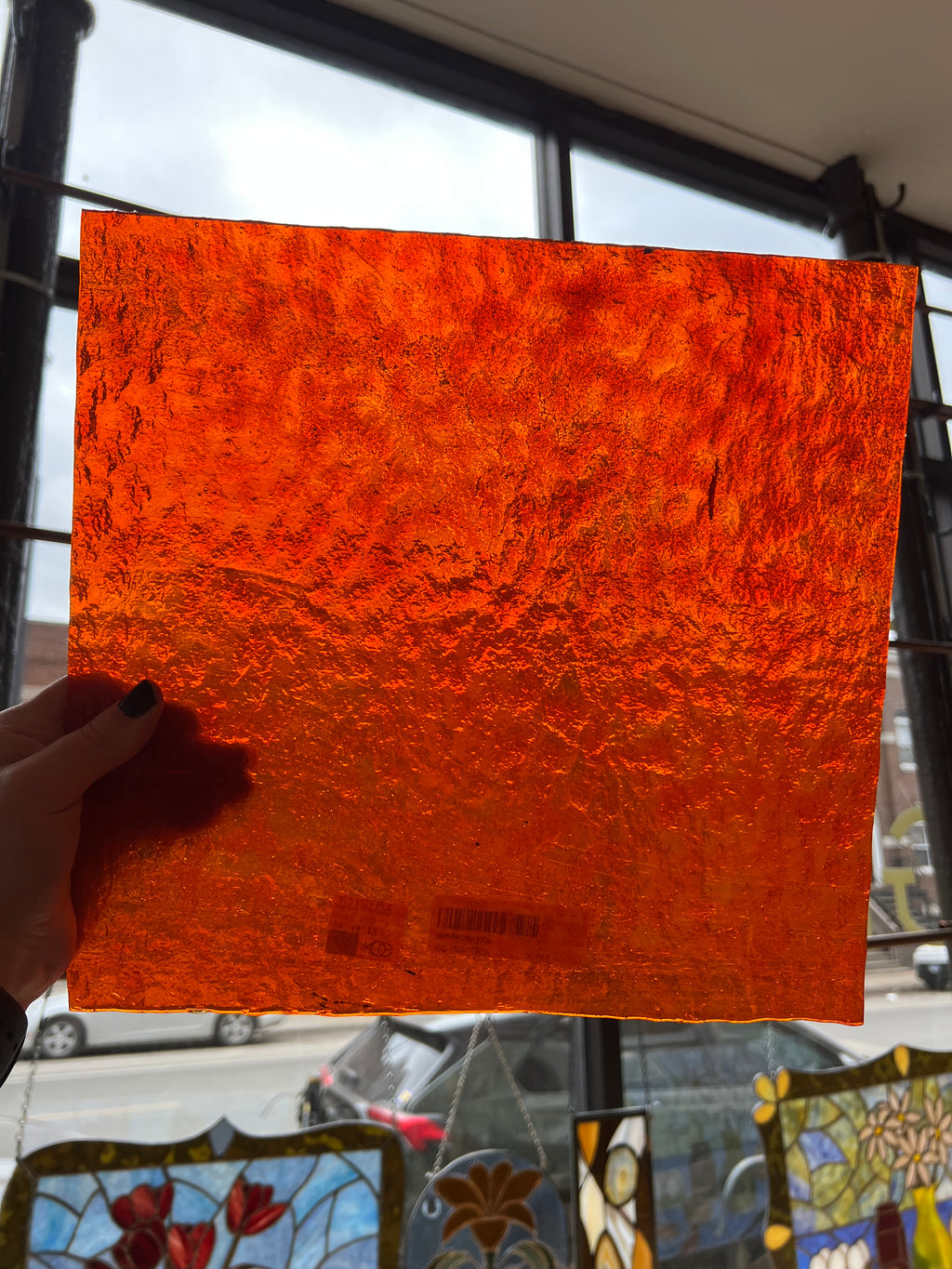 Hand holding an orange textured square of glass in front of a stained glass window