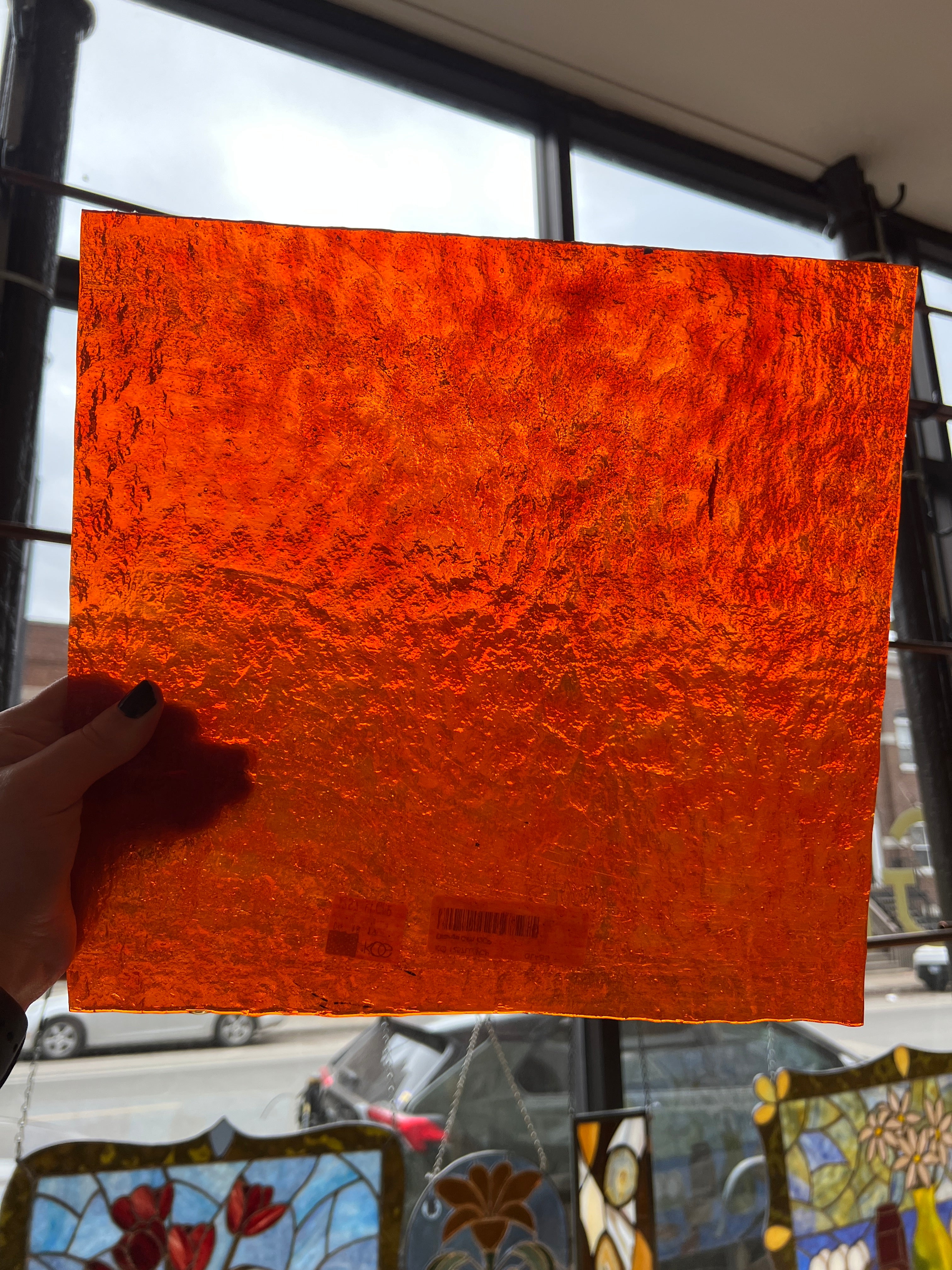 Hand holding an orange textured square of glass in front of a stained glass window