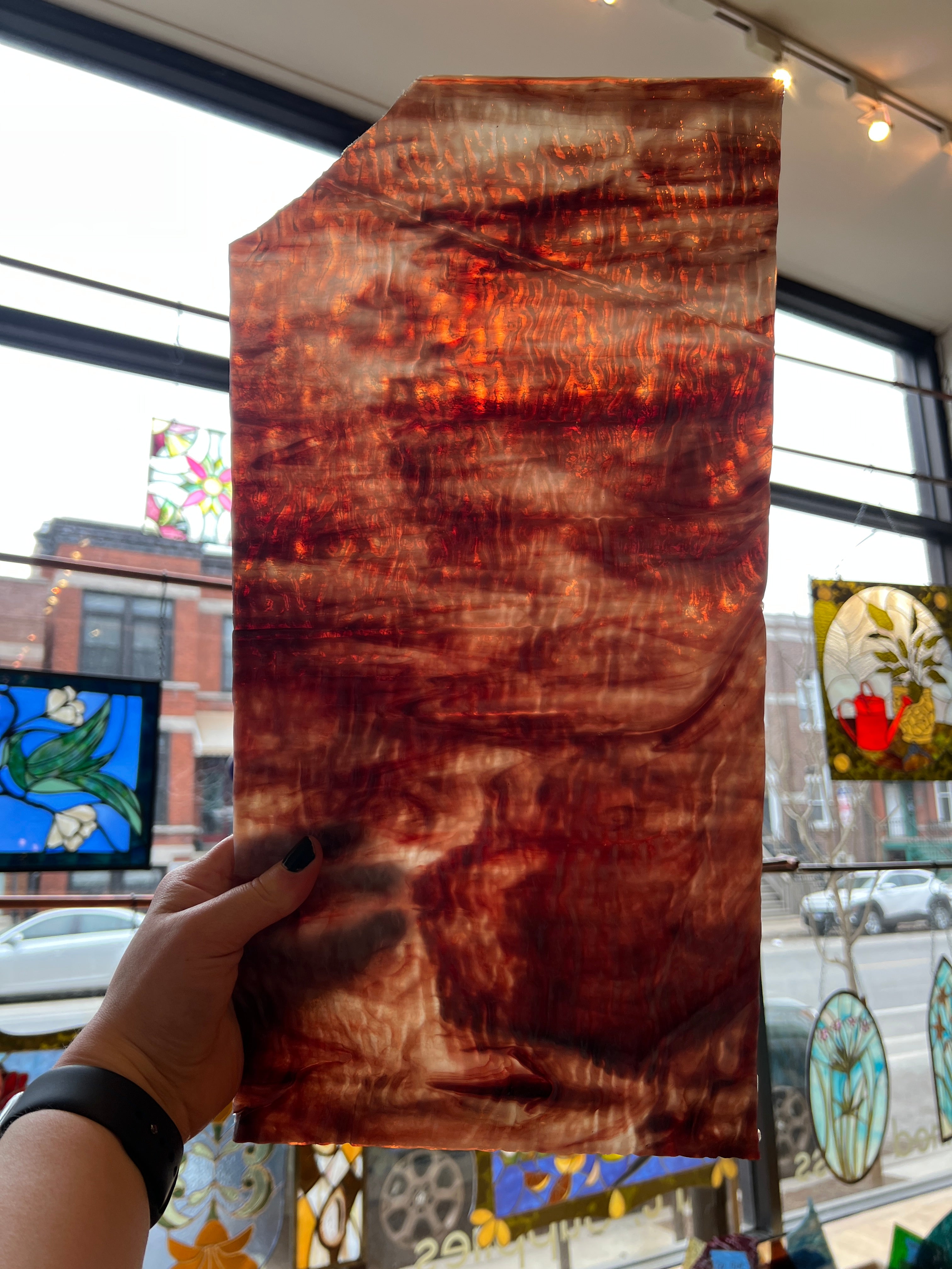 Hand holding a piece of glass with a distinctive textured pattern in front of a stained glass window.
