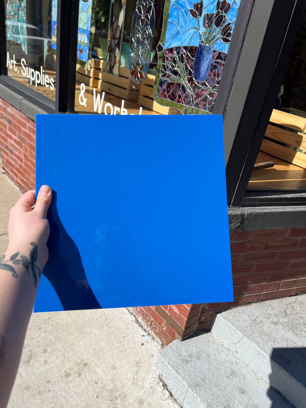 Hand holding a blue square of glass in front of a store window with stained glass displays.