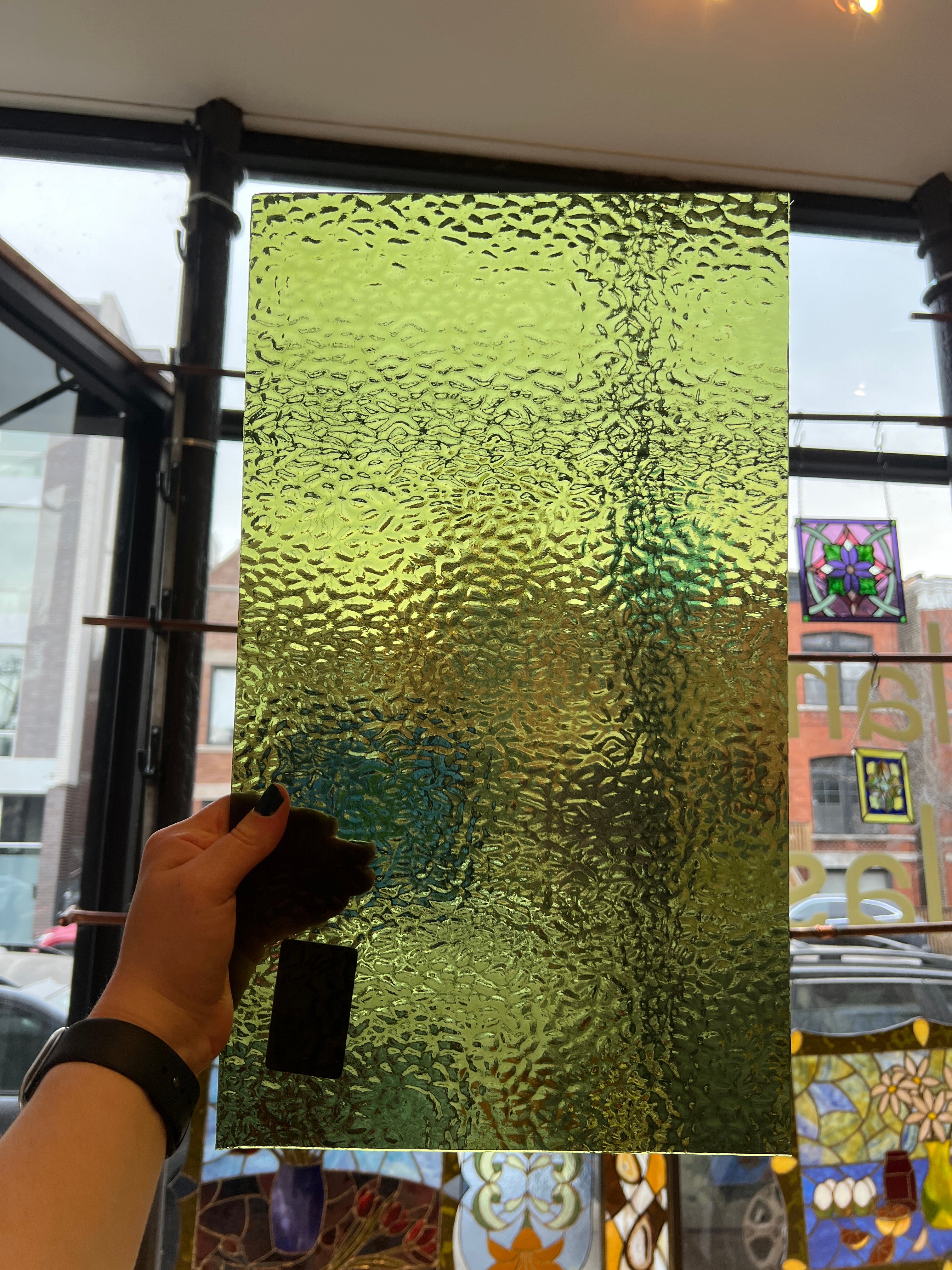 Hand holding a textured green glass panel with a blurred background