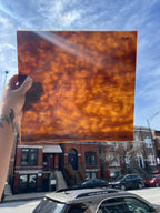 Person holding a rust colored piece of glass with urban street scene in the background